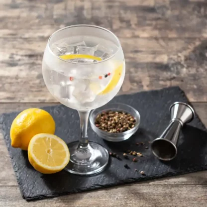 Gin Tonic con fetta di limone su tagliere nero - Cocktail rinfrescante e aromatico con note di lime e pepe